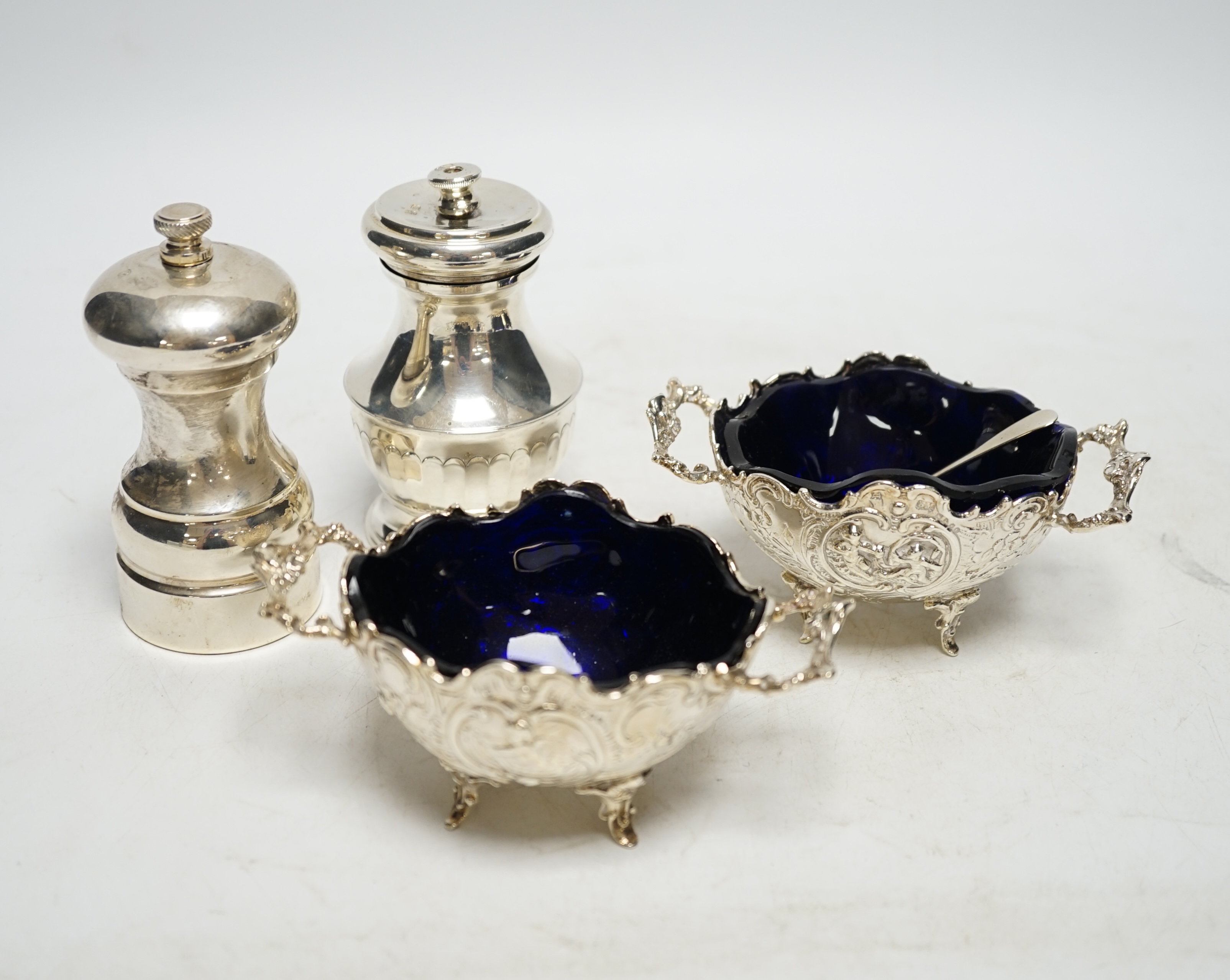 A pair of late 19th century Hanau silver two handled salts, with blue glass liners, import marks for Chester, 1899, with two associated spoons and two silver pepper mills. Condition - fair